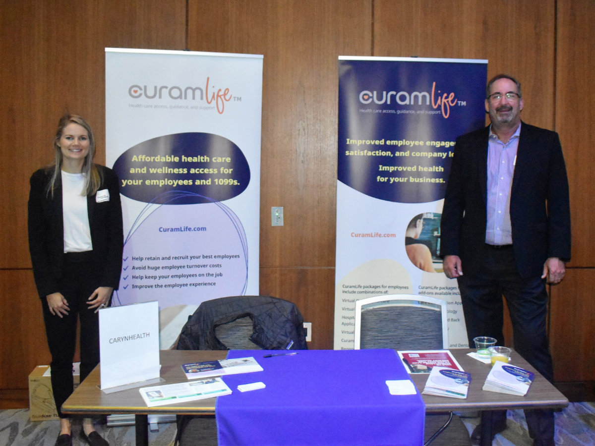 A pair of CuramLife reps stand poised for extensive conversation with attendees at the North Fulton Futures Summit during the North Fulton Chamber of Commerce Mayors Conference in Sandy Springs, GA, on Oct. 26.